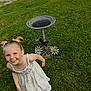 child, girl, smiling, dress, pigtails, grass, birdbath, flowers, outdoor, playful, motion_blur, happy, summer, nature, greenery, lawn, sunlight, cute, welcome_sign, metal_art