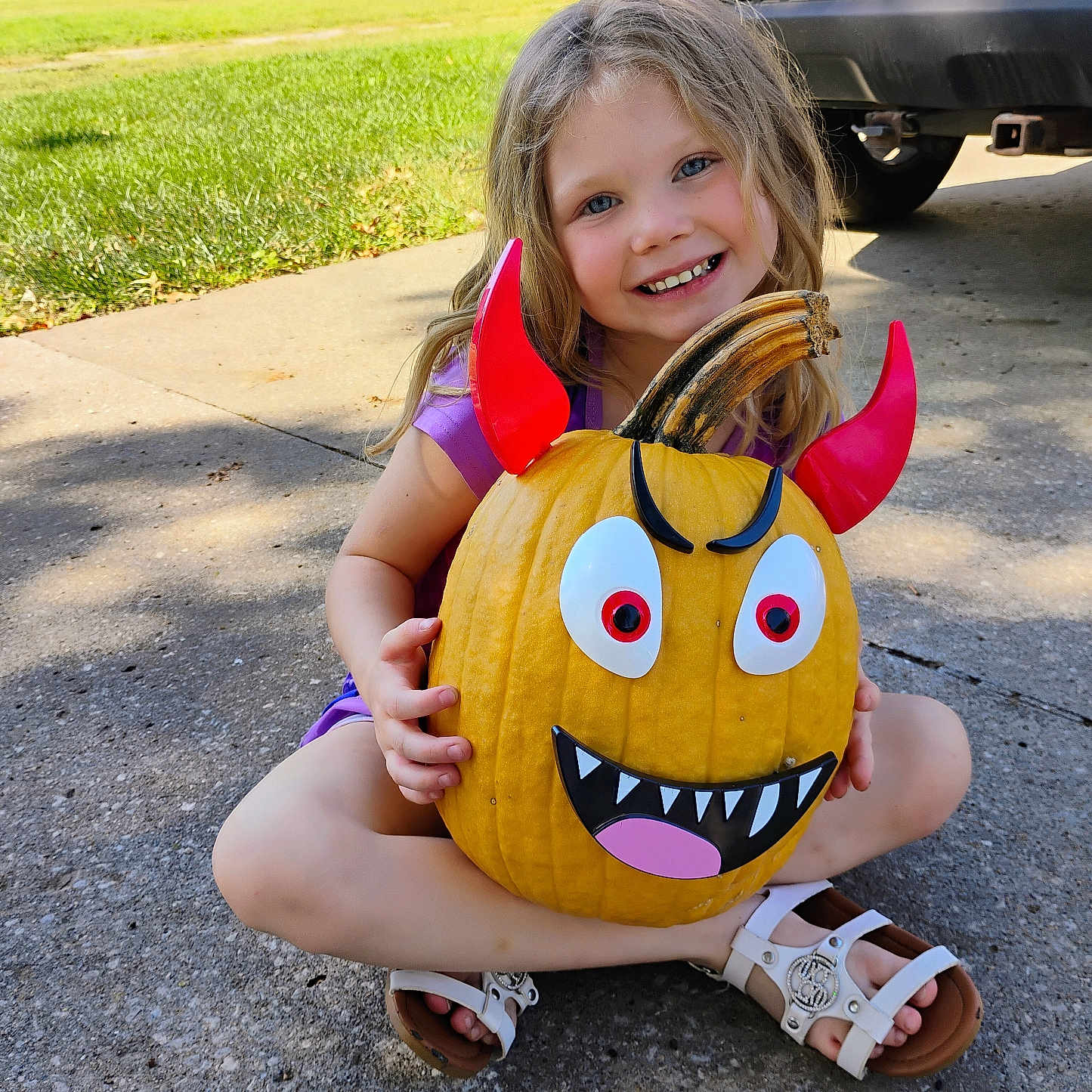 Hermonie is registered to the contest to win money with this photo: car, child, concrete, cute, daylight, decoration, devil_horns, driveway, fall, girl, grass, happy, holiday, house, outdoor, playful, pumpkin, purple_shirt, smiling, white_sandals