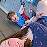 child, woman, smiling, outdoor, picnic, food, hotdog, snack, concrete, plate, shoe, blue_shirt, red_shorts, sunlight, happy, casual, bonding, family, relaxing, daytime