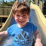 Elijah is registered to the contest to win money with this photo: child, boy, smile, slide, playground, outdoor, blue_shirt, jeans, happy, sunlight, hair, face, fun, recreation, daytime, park, metal_slide, handrail, casual_clothing, nature