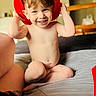 Elijah is registered to the contest to win money with this photo: toddler, child, smiling, red_hat, firefighter_hat, indoors, bed, skin, happy, cute, person, young_child, playful, sitting, bare_chest, home, furniture, light, portrait, fun