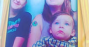 Zayden is registered to the contest to win money with this photo: adult, blue_background, cartoon_character, casual_clothing, child, chuck_e_cheese, family, fun, group, happy, holding, indoor, looking_up, people, photo_booth, plaid_shirt, portrait, smile, tattoo, yellow_frame