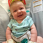 Sophia is registered to the contest to win money with this photo: baby, infant, smile, happy, onesie, mittens, baby_seat, pattern, rainbow, animal_design, indoor, cute, chubby_cheeks, person, child, plush, comfortable, colorful, head, face