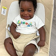 Sirkeino is registered to the contest to win money with this photo: baby, smiling, child, infant, seated, clothing, white_shirt, beige, cushion, baby_chair, happy, portrait, indoors, person, cute, shorts, skin, face, hair, young