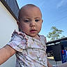 baby, child, outdoor, sky, onesie, floral_pattern, building, can, drink, curious, sitting, person, daylight, blue_sky, expression, face, head, arm, leg, tree