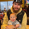 Linley joined the competition — help win amazing prizes! baby, man, beard, cap, smile, happy, restaurant, table, chair, indoor, clothing, person, face, hands, casual, hoodie, window, light, seated, background