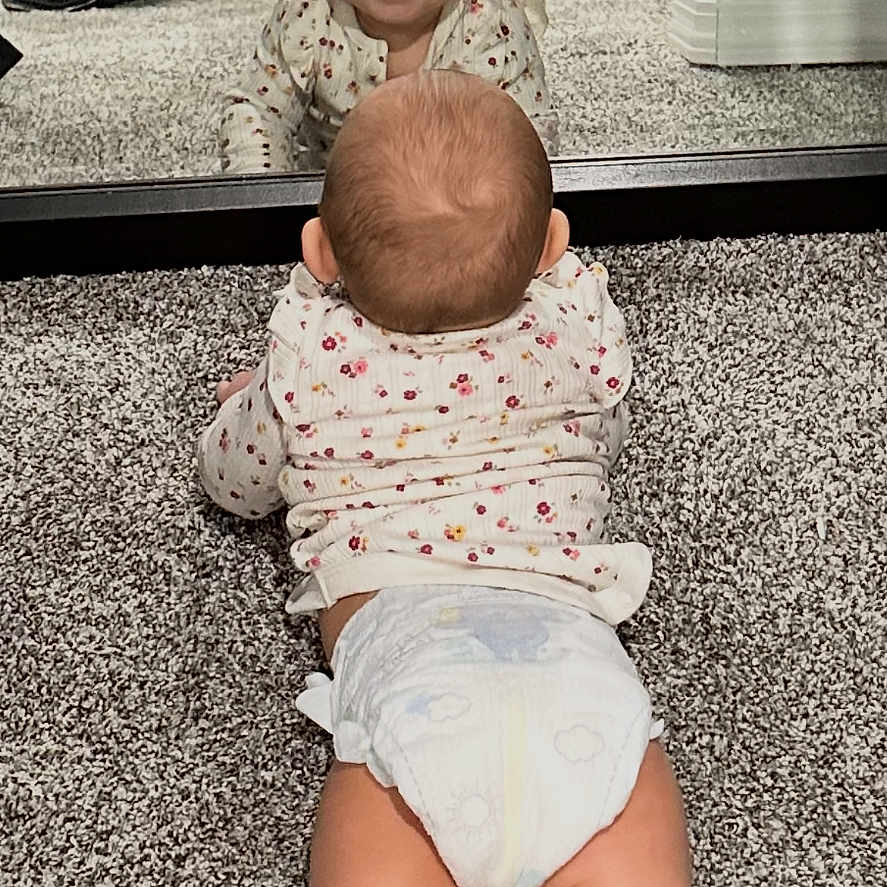 Linley is registered to the contest to win money with this photo: baby, diaper, mirror, reflection, carpet, indoor, smiling, child, floor, person, clothing, footwear, adult, happy, crawling, head, legs, toes, room, wall
