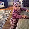 toddler, child, purple_outfit, headband, daisy_pattern, indoor, living_room, wooden_floor, rug, couch, curious, standing, baby, person, clothing, furniture, home, cute, portrait, smiling