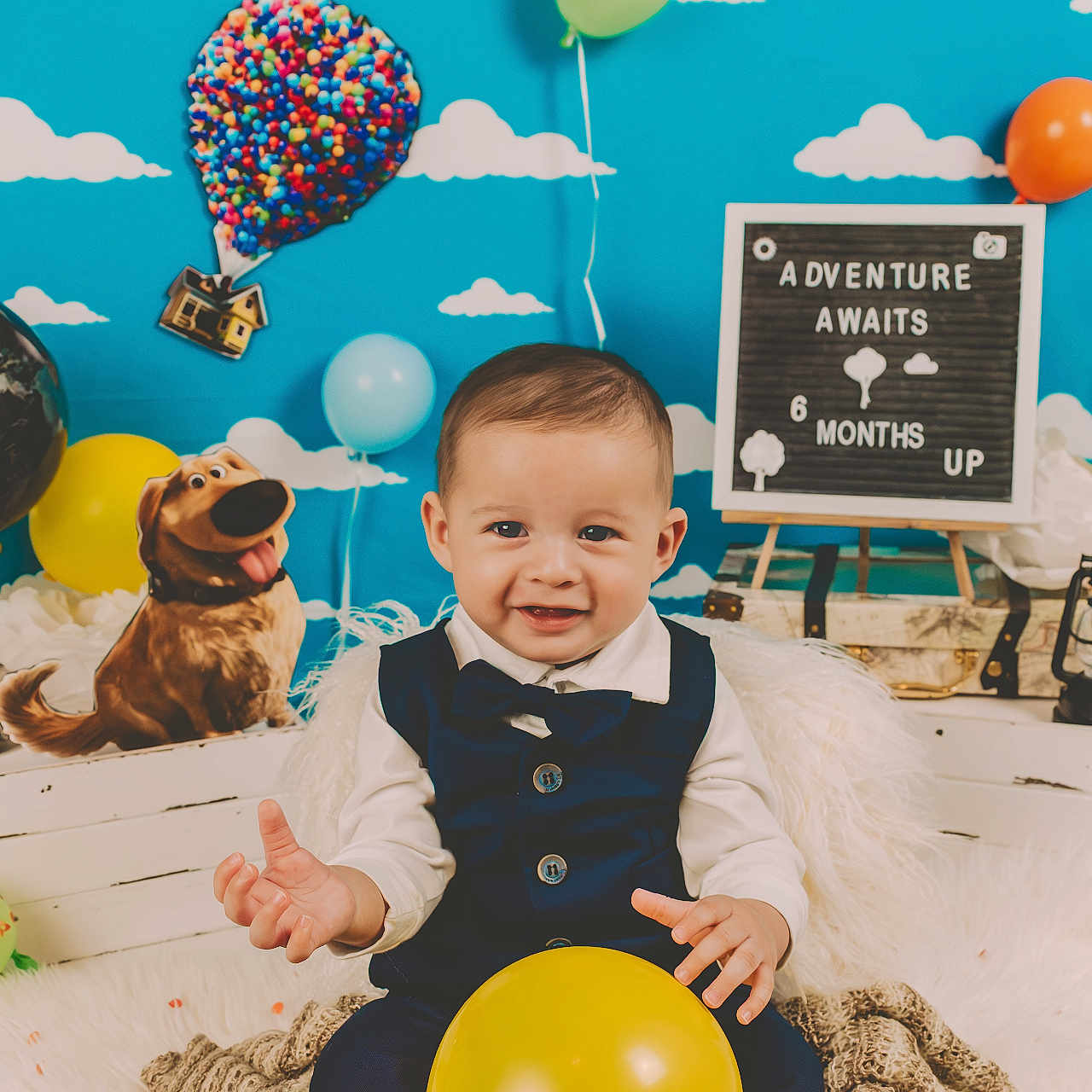 Natanael is registered to the contest to win money with this photo: baby, child, smiling, balloon, blue_sky, clouds, globe, dog_cutout, decor, sign_board, milestone, vest, bow_tie, sitting, indoor, colorful, celebration, toy, portrait, happy