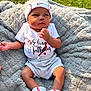 baby, infant, clothing, hat, socks, blanket, outdoor, grass, portrait, cute, soft_texture, sunlight, baseball_theme, headwear, shorts, person, young_child, baby_boy, resting, casual