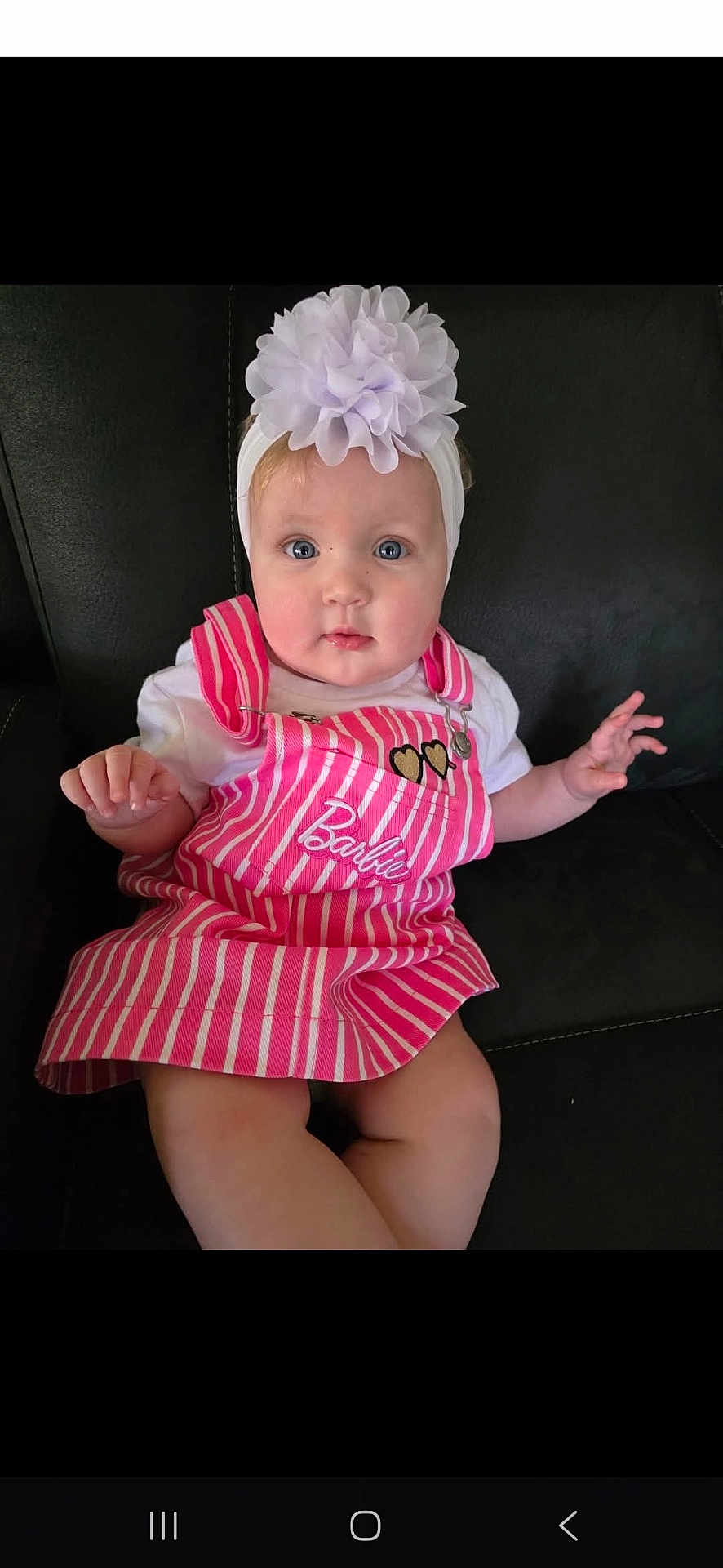 Amelia is registered to the contest to win money with this photo: baby, child, girl, headband, flower, pink_dress, striped_clothing, barbie, heart_patch, sitting, couch, indoor, cute, portrait, blue_eyes, white_shirt, infant, hand, face, looking