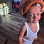 toddler, child, indoors, floor, hat, knit_hat, orange, barefoot, white_shirt, tank_top, living_room, couch, wooden_floor, furniture, small_chair, table, person, home, blur, casual