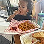 child, curly_hair, eating, fried_food, french_fries, takeout_container, table, sippy_cup, indoor, home, treadmill, chair, food, snack, person, meal, plastic_cup, curly_hair_child, casual, ketchup