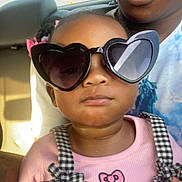 Starr is registered to the contest to win money with this photo: child, toddler, sunglasses, heart_shaped, pink, black_and_white, checkered, overalls, car_interior, adult, person, fashion, cute, serious, closeup, portrait, seat, hair_bows, casual, sunlight