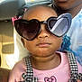 child, toddler, sunglasses, heart_shaped, pink, black_and_white, checkered, overalls, car_interior, adult, person, fashion, cute, serious, closeup, portrait, seat, hair_bows, casual, sunlight