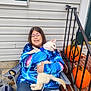 Stitch is registered to the contest to win money with this photo: person, dog, hoodie, blue_clothing, pumpkin, porch, stairs, railing, smile, glasses, leash, outdoor, fall, brick, concrete, plastic_bag, casual, pet, holding, festive