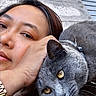 person, cat, gray_cat, yellow_eyes, watch, patterned_clothing, shoulder, close_up, outdoor, wooden_background, metal_slats, pet, animal, cozy, affection, resting_cat, face, portrait, human, companion