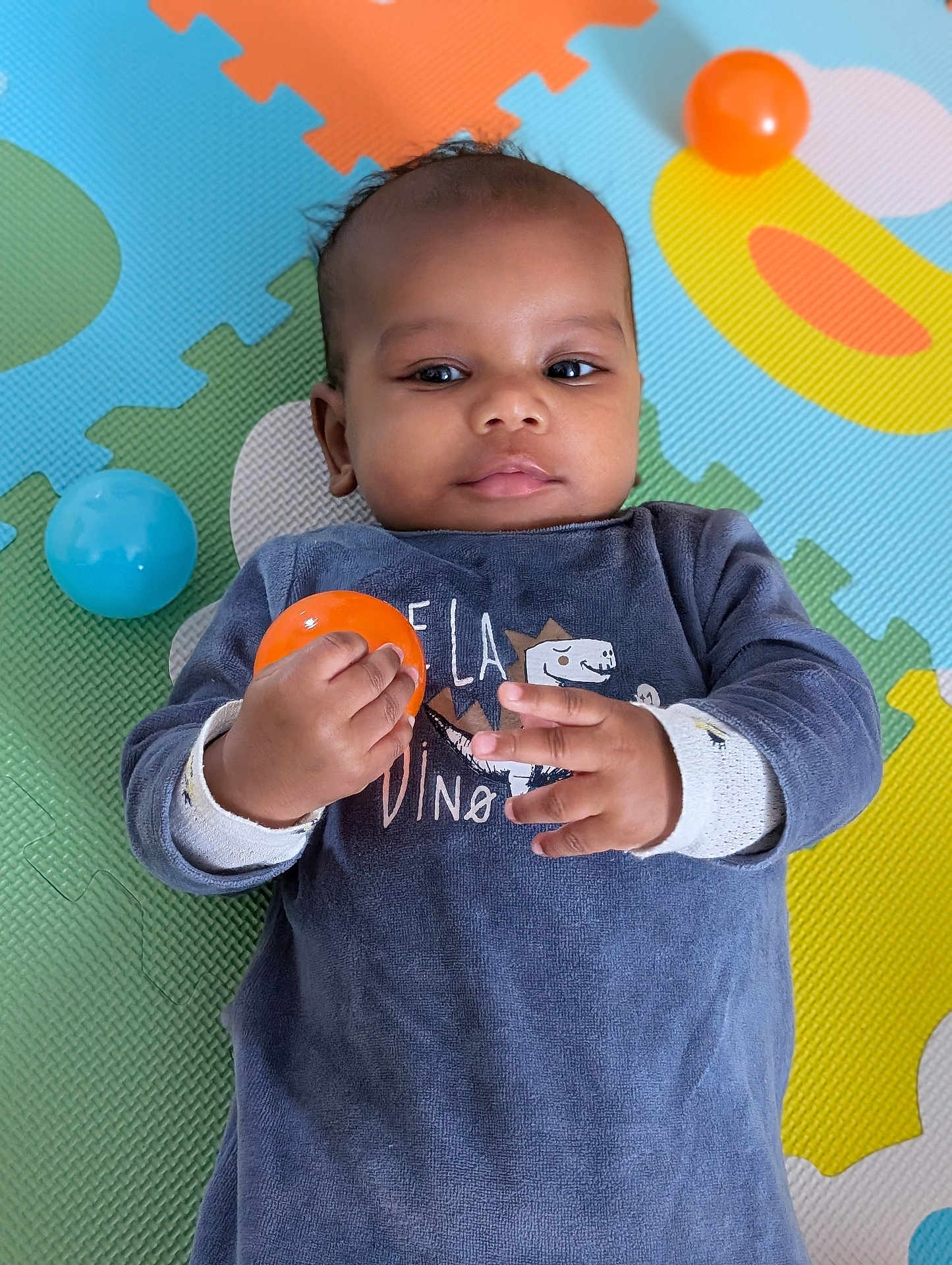 Heaven a rejoint le concours — aidez-le/la à gagner de superbes lots ! baby, child, infant, play_mat, colorful, toy_ball, orange_ball, blue_ball, clothing, laying_down, hands, face, curious, indoor, soft_texture, patterned_background, young_child, cute, portrait, casual