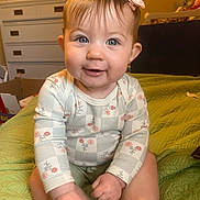 Aurora joined the competition — help win amazing prizes! baby, child, smiling, blue_eyes, pink_bow, long_sleeve_shirt, floral_pattern, green_quilt, bedroom, dresser, furniture, indoor, person, cute, infant, sitting, happy, skin, head, photography