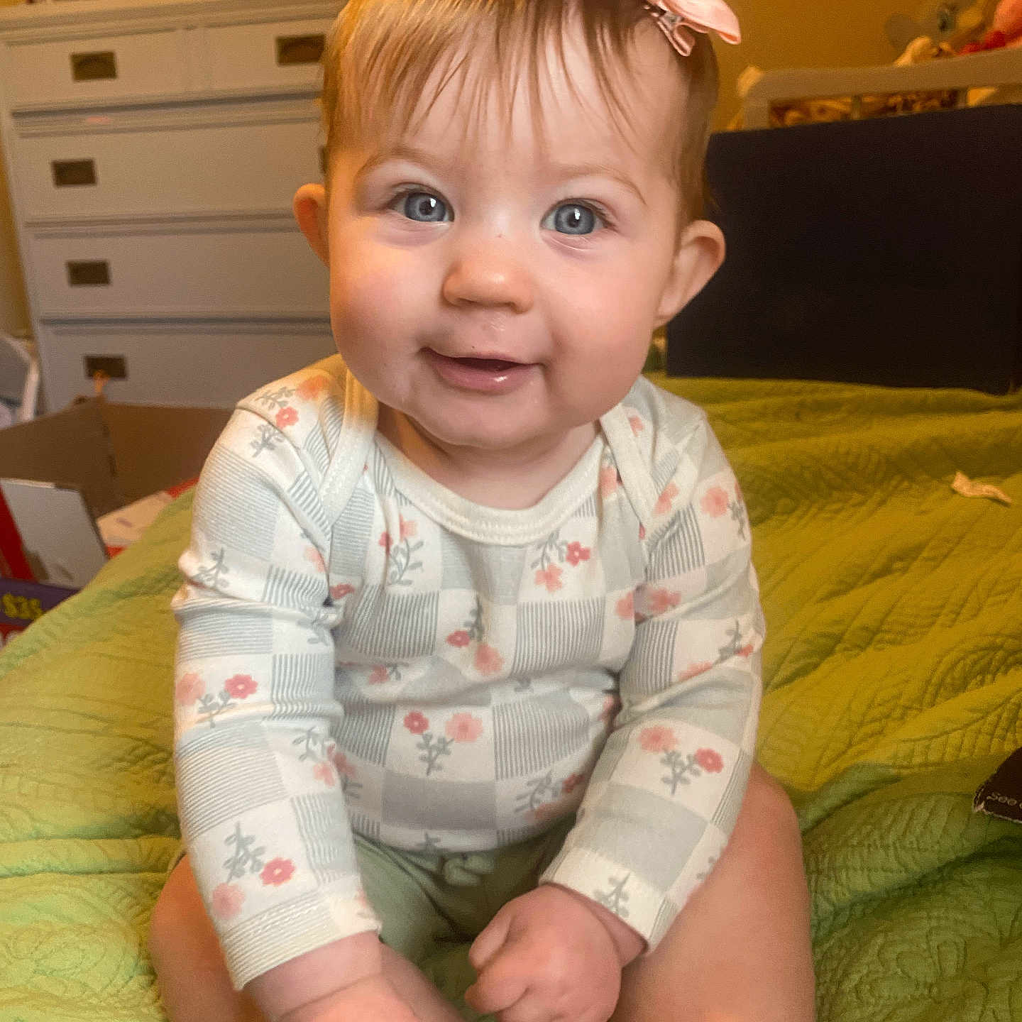 Aurora joined the competition — help win amazing prizes! baby, child, smiling, blue_eyes, pink_bow, long_sleeve_shirt, floral_pattern, green_quilt, bedroom, dresser, furniture, indoor, person, cute, infant, sitting, happy, skin, head, photography