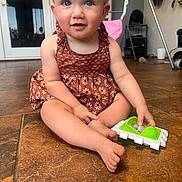 Hazel joined the competition — help win amazing prizes! baby, barefoot, child, curious, dress, face, feet, floor, hands, home, indoor, light, patterned_clothing, person, playtime, portrait, sitting, smiling, toddler, toy