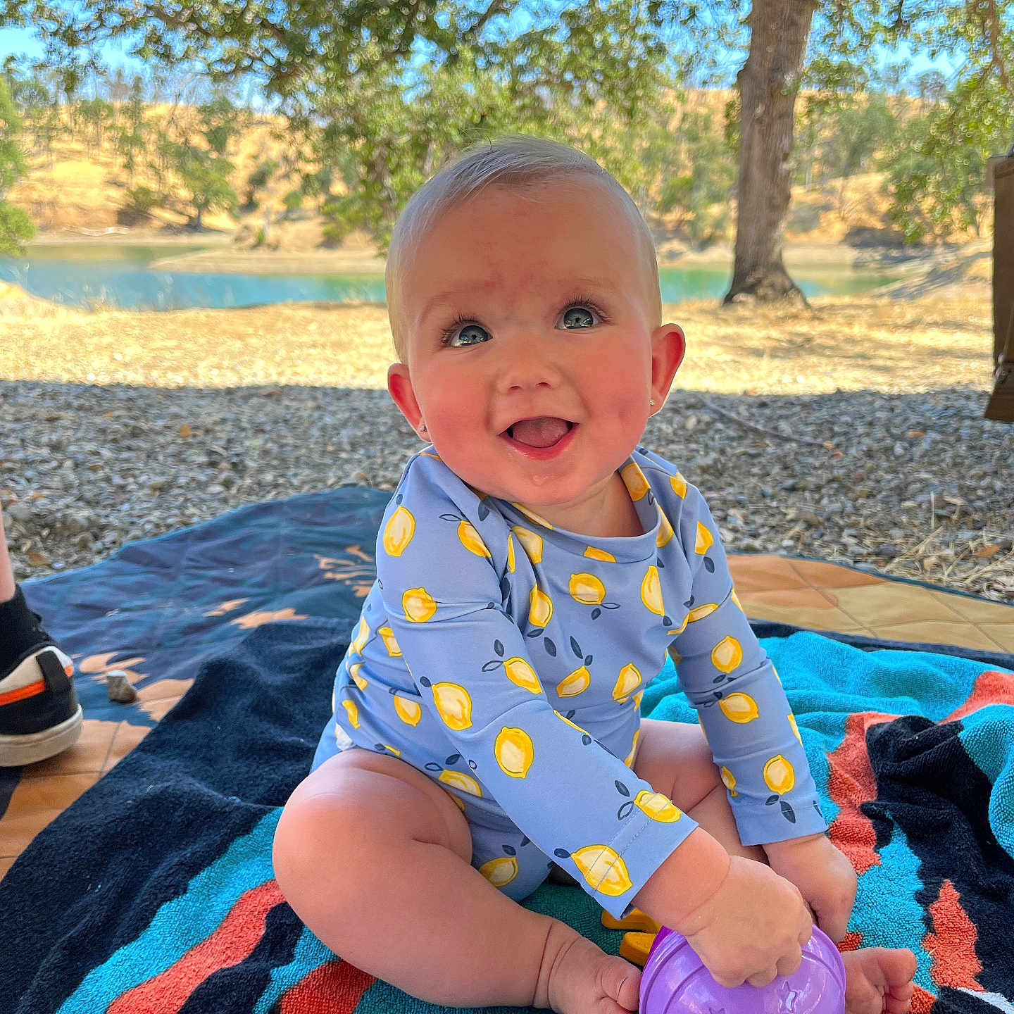 Hazel is registered to the contest to win money with this photo: baby, blue_eyes, child, grass, happy, lake, legs, nature, outdoor, person, picnic, playing, shorts, smiling, sneakers, summer, sunlight, towel, toy, tree