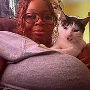 Jack joined the competition — help win amazing prizes! black_and_white_cat, casual_clothing, cat, cozy, curtain, expression, face, furniture, glasses, hair, holding, home, indoor, person, pet, portrait, seated, smiling, woman, yellow_wall