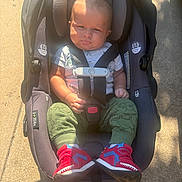 Roy joined the competition — help win amazing prizes! baby, car_seat, child, sneakers, green_pants, sunlight, outdoor, concrete, seat_belt, infant, clothing, footwear, sitting, person, casual, daylight, shadow, safety, cute, portrait