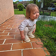 Eden a rejoint le concours — aidez-le/la à gagner de superbes lots ! toddler, child, crouching, brick_patio, grass, fence, outdoor, sneakers, long_sleeve_shirt, pants, smile, suburban, yard, greenery, daylight, cloudy_sky, person, young_child, cute, casual_clothing