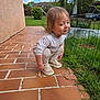 toddler, child, crouching, brick_patio, grass, fence, outdoor, sneakers, long_sleeve_shirt, pants, smile, suburban, yard, greenery, daylight, cloudy_sky, person, young_child, cute, casual_clothing