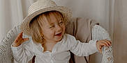 Eden participe au concours pour gagner de l'argent avec cette photo : toddler, child, hat, straw_hat, white_shirt, beige_pants, barefoot, wicker_chair, blanket, smiling, happy, sitting, indoors, neutral_background, playful, cute, portrait, young_child, clothing, baby