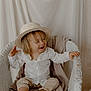 toddler, child, hat, straw_hat, white_shirt, beige_pants, barefoot, wicker_chair, blanket, smiling, happy, sitting, indoors, neutral_background, playful, cute, portrait, young_child, clothing, baby