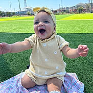Azul joined the competition — help win amazing prizes! baby, child, smiling, yellow_outfit, headband, blanket, grass, outdoor, sunny, happy, sitting, sock, kneeling, cute, portrait, daylight, field, playful, infant, expression