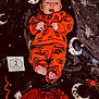 baby, infant, orange_clothing, pumpkin_pattern, halloween, blanket, moon, stars, witch, spider, jack_o_lantern, feet, hands, face, smile, months_marker, holiday, festive, cute, lying_down