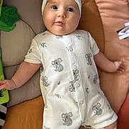 Delaney is registered to the contest to win money with this photo: baby, infant, child, onesie, headband, koala_pattern, cushion, blanket, soft_toy, cute, smiling, indoor, lying_down, white_clothing, baby_garment, adorable, baby_legwear, comfort, young_child, portrait