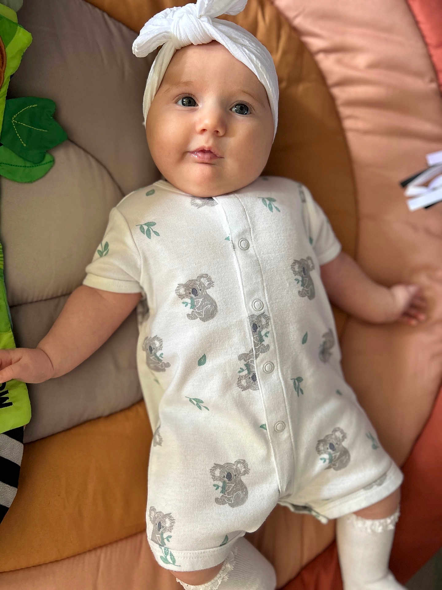 Delaney is registered to the contest to win money with this photo: baby, infant, child, onesie, headband, koala_pattern, cushion, blanket, soft_toy, cute, smiling, indoor, lying_down, white_clothing, baby_garment, adorable, baby_legwear, comfort, young_child, portrait