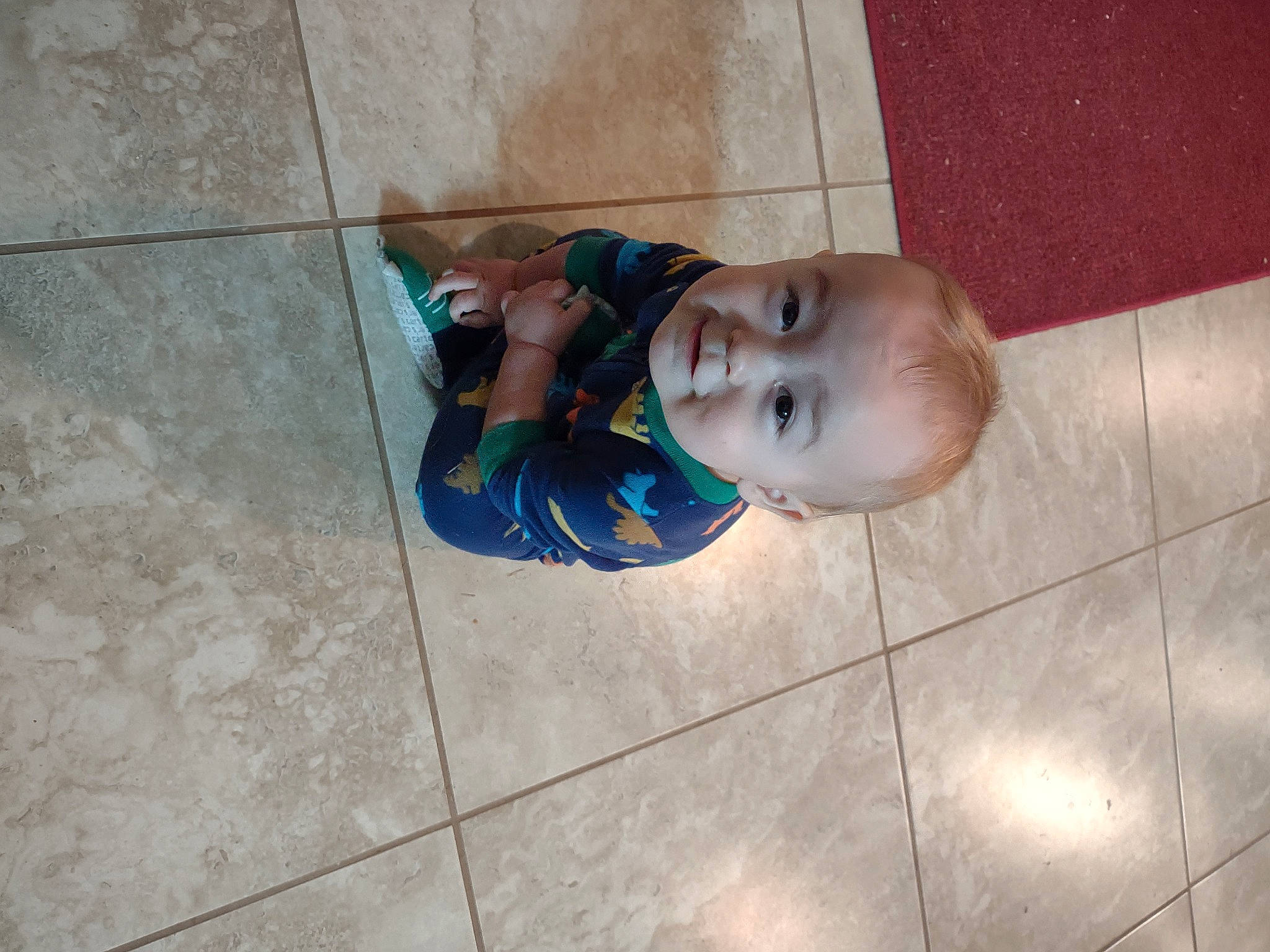 Hagen is registered to the contest to win money with this photo: art, baby, child, concrete, eye, face, floor, flooring, foot, human_leg, pattern, person, road_surface, sidewalk, sitting, smile, tile, toddler, wall, water