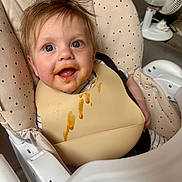 Reggie is registered to the contest to win money with this photo: baby, high_chair, bib, messy, food, smiling, blue_eyes, hair, polka_dot, cushion, feeding, infant, cute, happy, indoor, child, face, mouth_open, seat, fan