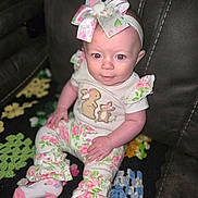 Lilith is registered to the contest to win money with this photo: baby, child, infant, headband, bow, floral_clothing, pajamas, couch, crocheted_blanket, colorful_blanket, sitting, cute, portrait, indoor, person, smile, face, hand, footwear, pink