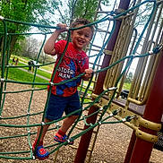 Andre joined the competition — help win amazing prizes! child, playground, climbing, rope_net, spiderman_shirt, smiling, outdoor, trees, wood_chips, play_equipment, shorts, shoes, happy, person, daylight, nature, fun, park, greenery, activity