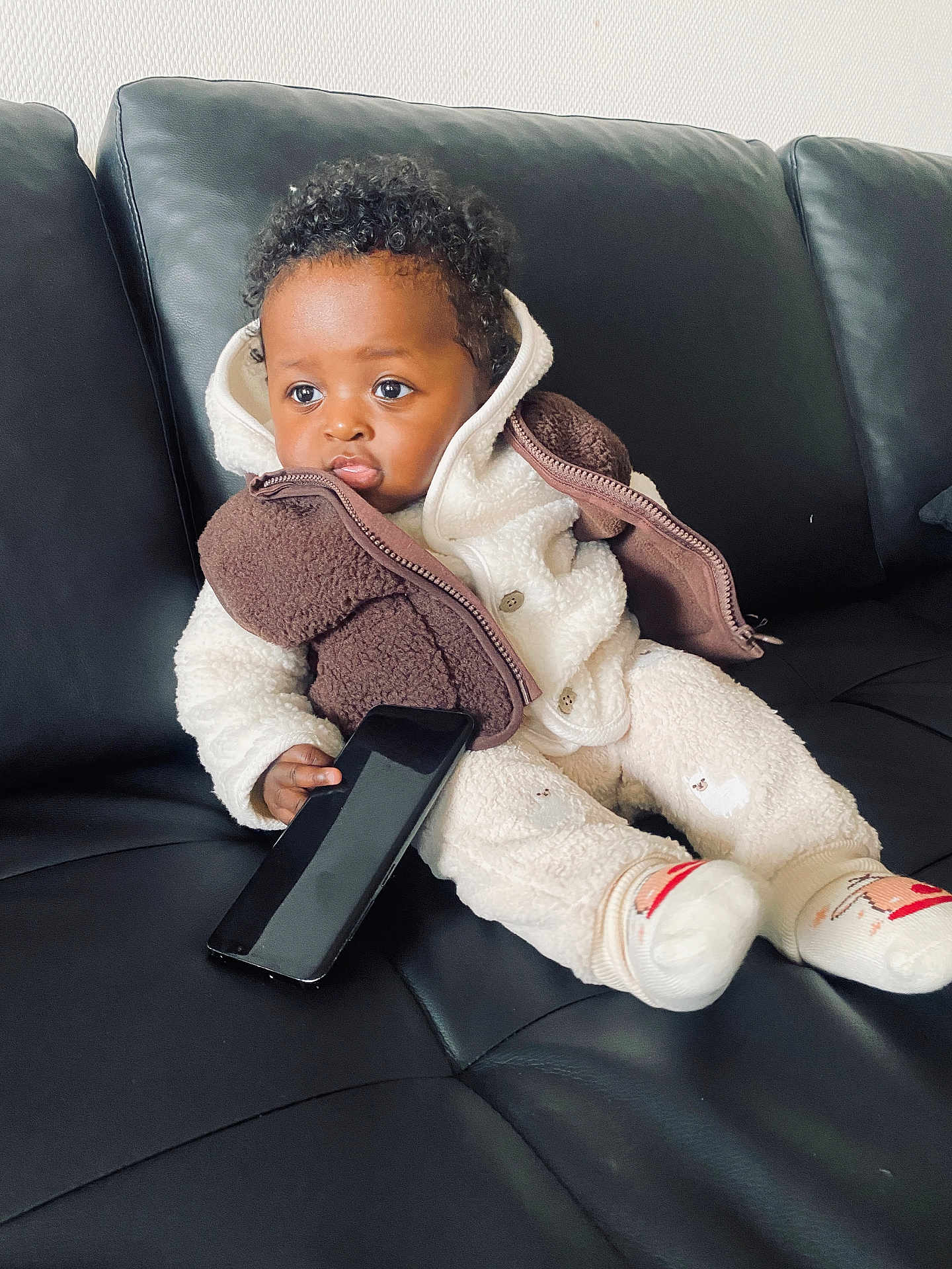 Davi a rejoint le concours — aidez-le/la à gagner de superbes lots ! toddler, child, baby, couch, leather, black, phone, smartphone, clothing, jacket, socks, curly_hair, indoor, seated, pout, cute, cozy, warm, expression, portrait