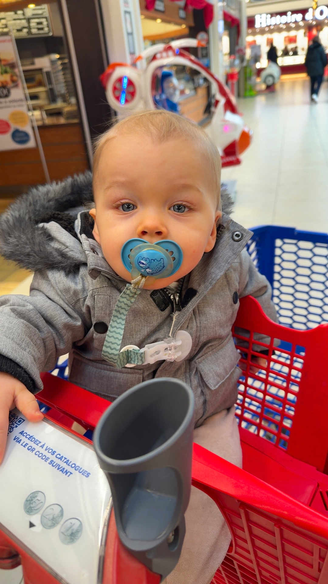Noah a rejoint le concours — aidez-le/la à gagner de superbes lots ! child, baby, toddler, pacifier, pacifier_clip, shopping_cart, shopping_mall, coat, fur_hood, blue_eyes, face, close_up, sitting, hand, retail_store, portrait, bokeh, seat, toy_ride, winter_clothing