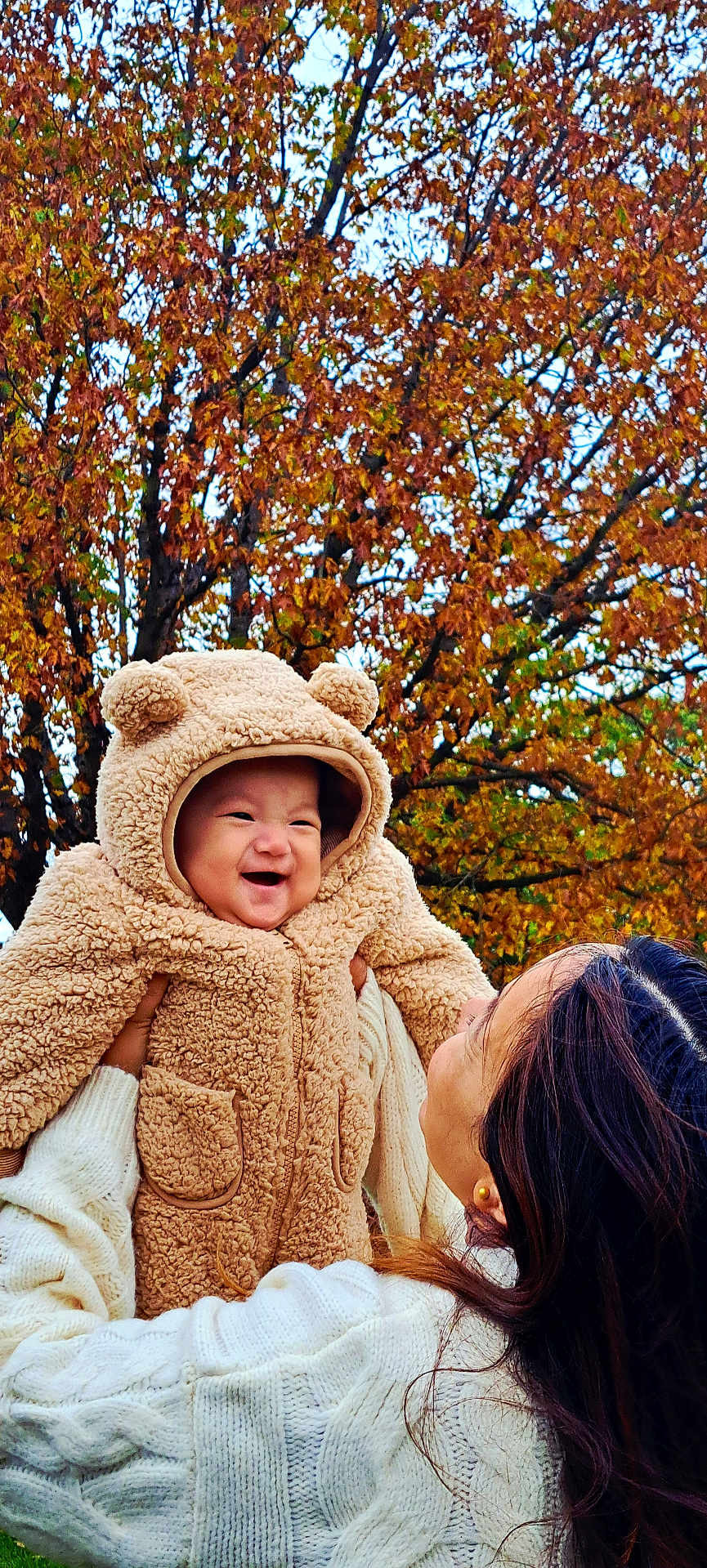 Saangshi is registered to the contest to win money with this photo: baby, child, adult, autumn, fall_leaves, tree, outdoor, smile, happy, coat, hood, bear_ears, warm_clothing, person, nature, seasonal, holding, joy, family, portrait