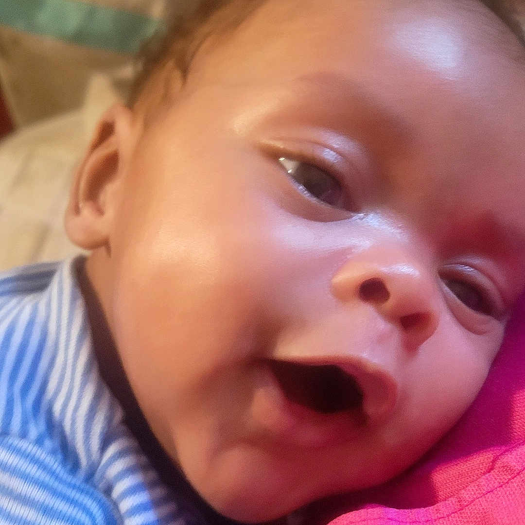 Ozias joined the competition — help win amazing prizes! baby, infant, close_up, face, smiling, striped_clothing, blue, pink, skin, happy, snuggling, soft_lighting, indoors, portrait, child, cuteness, expression, head, cheeks, young