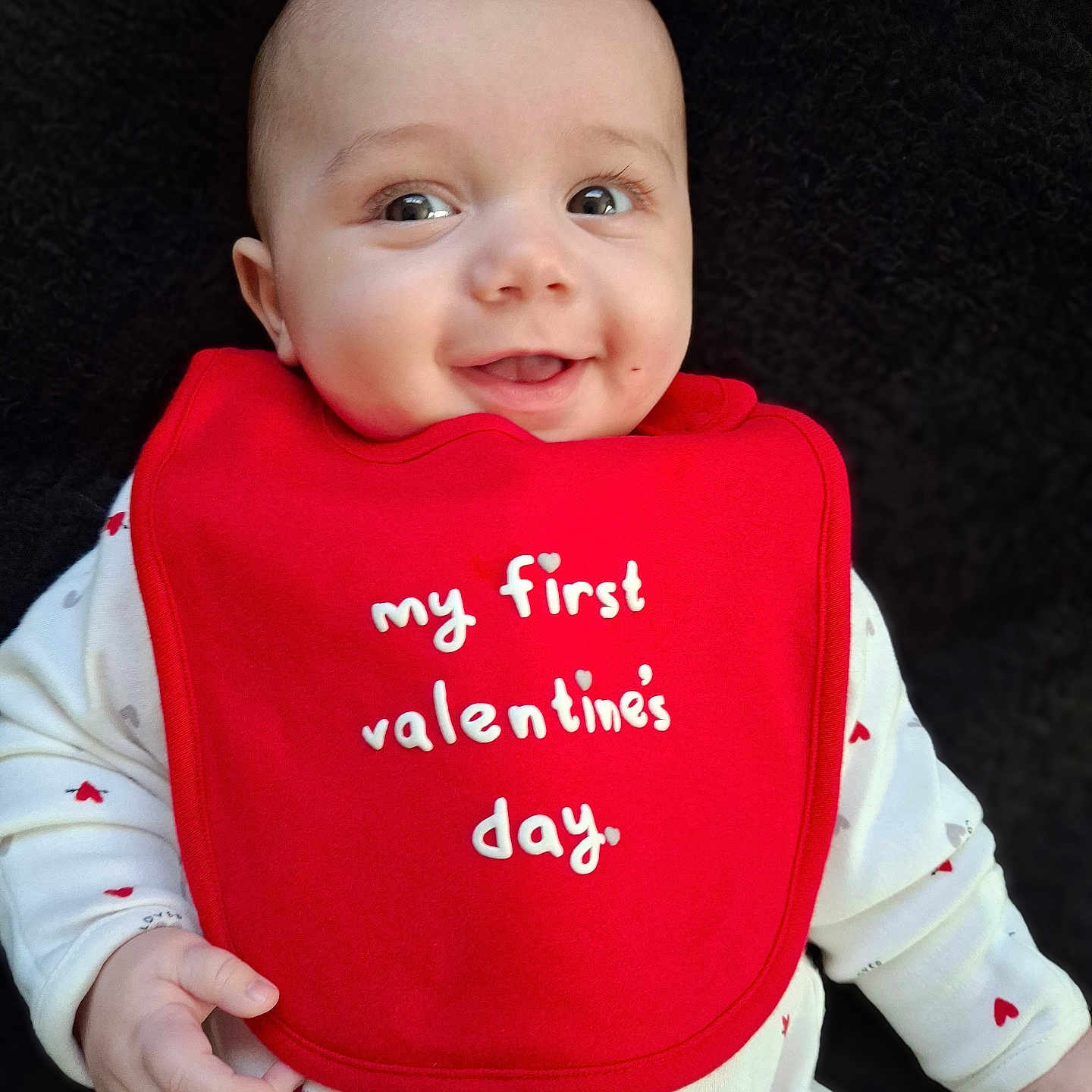 Nathanial is registered to the contest to win money with this photo: baby, celebration, child, closeup, clothing, cute, face, hand, happy, hearts, holiday, indoor, infant, person, portrait, red_bib, smile, valentines_day, white_outfit, young_child