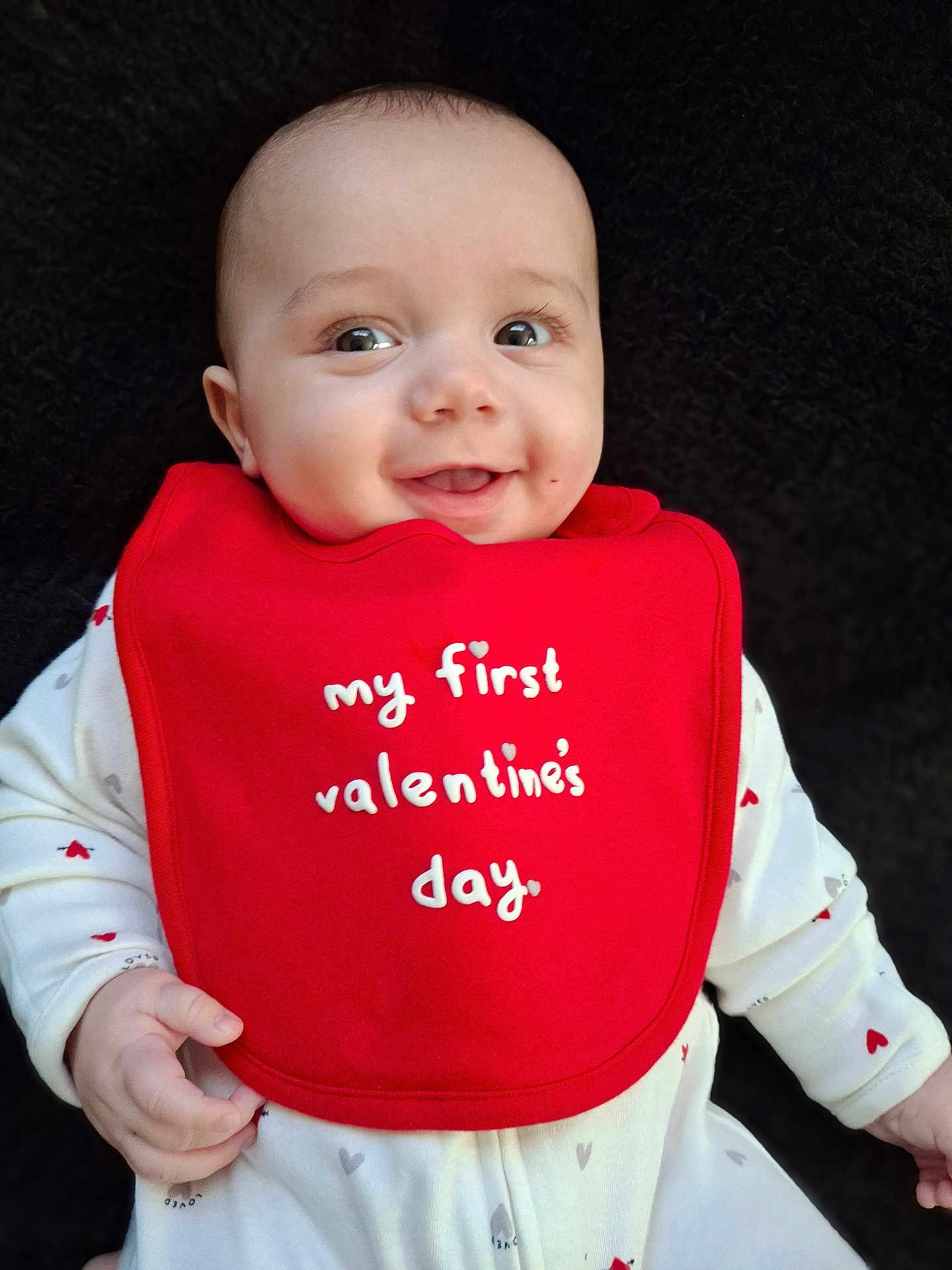 Nathanial is registered to the contest to win money with this photo: baby, infant, smile, red_bib, valentines_day, white_outfit, hearts, cute, child, portrait, happy, face, hand, clothing, closeup, indoor, person, young_child, celebration, holiday