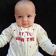 Nathanial is registered to the contest to win money with this photo: baby, infant, onesie, heart_patterns, white_clothing, red_hearts, gray_hearts, lying_down, black_background, cute, smiling, face, head, skin, child, portrait, closeup, baby_girl, baby_boy, soft_texture