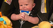 Wesley is registered to the contest to win money with this photo: baby, infant, car_seat, plush_toys, tuxedo_outfit, smiling, cute, child, indoor, seatbelt, toy, yellow_toy, blue_toy, orange_toy, clothing, head, face, hands, person, portrait