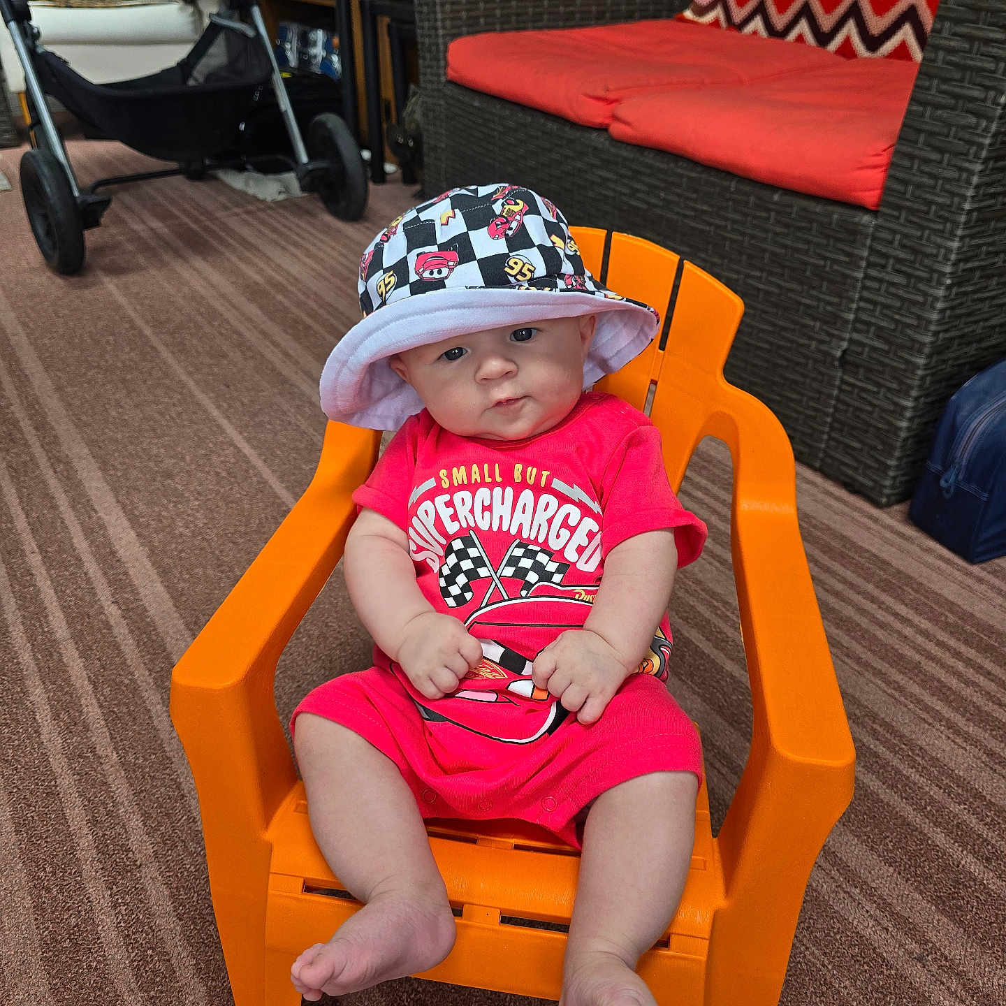 Wesley joined the competition — help win amazing prizes! baby, child, indoor, orange_chair, bucket_hat, red_outfit, car_design, stroller, carpet, wicker_furniture, cushions, living_room, cute, sitting, person, foot, face, hat, toy, casual