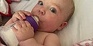 Poppy is registered to the contest to win money with this photo: baby, bottle, milk, blanket, pink, floral, curious, face, hand, bed, pillow, soft, infant, child, indoors, cute, feeding, sleeping_area, resting, person
